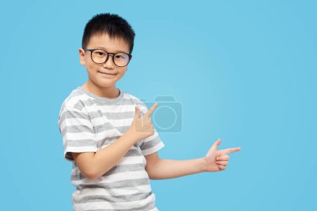 Photo for Kid with fingers pointing and presenting, wearing eyeglasses on blue background - Royalty Free Image