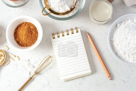 Photo for Notebook and pen with baking ingredients, flour, brown sugar, milk on marble table, top view - Royalty Free Image
