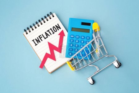Concepto de inflación y aumento de precios al consumidor, palabra de inflación y gráfico de aumento rojo en el cuaderno con calculadora en el carrito de la compra sobre fondo azul