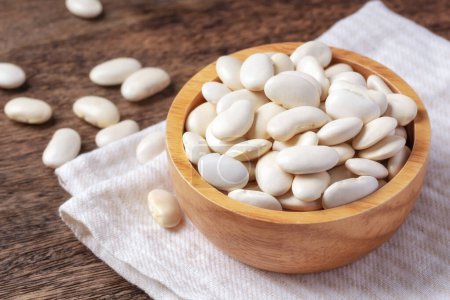 Raw white beans in bowl on linen cloth, closeup
