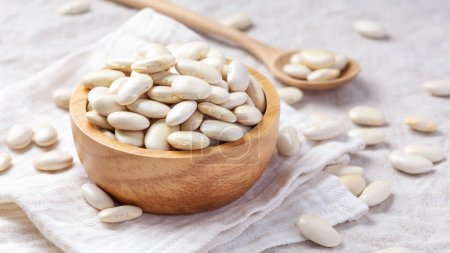 Heap of white beans in wood bowl with spoon on linen cloth background, with copy space