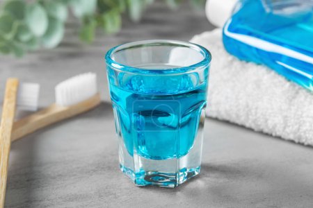 Photo for Mouthwash in glass cup, closeup with toothbrush and towel on grey table - Royalty Free Image