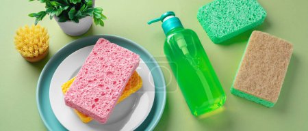 Foto de Esponjas de limpieza natural y cepillo con líquido de lavado de platos sobre fondo verde - Imagen libre de derechos