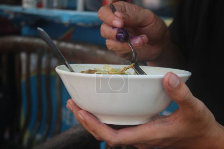 Indonesier isst fröhlich Hühnernudelsuppe an einem Imbissstand