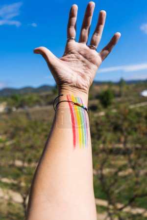 Personne méconnaissable avec bracelet et couleurs de la protestation LGTBI + drapeau LGTBI conceptuel