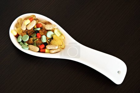 Foto de Ceramic spoon with colored pills, dietary supplements on a dark background. The topic of health care, treatment and prevention of diseases. - Imagen libre de derechos
