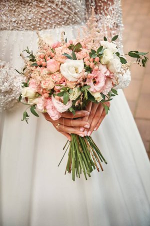 Foto de The bride holds a wedding bouquet in her hands. Festive theme. - Imagen libre de derechos