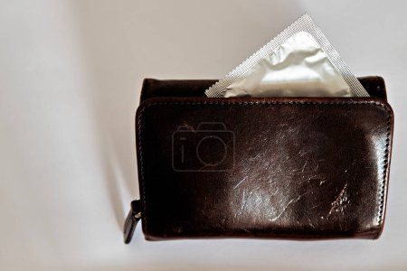 Foto de Condón medio asomándose de una billetera marrón sobre un fondo blanco. Vista lateral. El concepto de sexo seguro - Imagen libre de derechos
