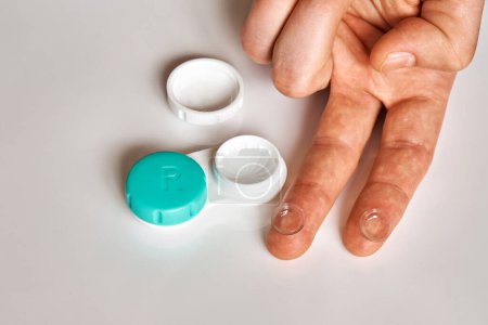 Foto de Un hombre sostiene lentes de contacto en sus dedos en el fondo de un recipiente para ellos. El tema de la medicina y la atención médica. - Imagen libre de derechos