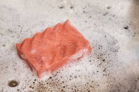 Ein pinkfarbener Küchenschaumschwamm ruht in einer Edelstahl-Schaumspüle.