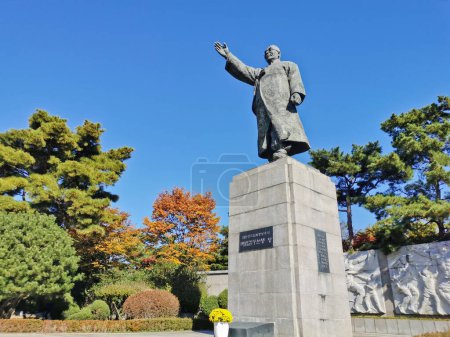 Foto de SEÚL, COREA DEL SUR - 26 DE OCTUBRE DE 2022: Estatua de Kim Gu (Kim Koo) levanta su mano derecha en la Plaza Baekbeom en Namsan Mountain Park con árboles coloridos follaje en otoño. - Imagen libre de derechos