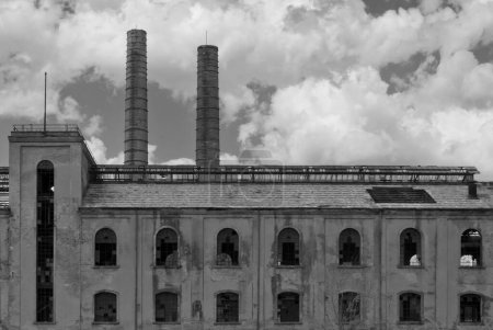 Téléchargez les photos : Vue monochromatique d'une ancienne usine abandonnée avec deux cheminées et de nombreuses fenêtres avec des lunettes cassées - en image libre de droit