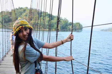 Foto de Viajeros tailandeses fotógrafas visitan y posan retrato toman foto en puente colgante de madera cruzando lago a isla en la presa Kaeng Krachan y el Parque Nacional en Phetchaburi, Tailandia - Imagen libre de derechos
