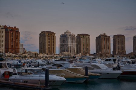 Téléchargez les photos : Doha, Qatar- 1 mars 2024 : Marina de Porto Arabia au coucher du soleil perlé montrant des yachts de luxe et des bateaux amarrés à la marina avec des bâtiments résidentiels en arrière-plan. - en image libre de droit