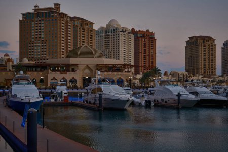 Téléchargez les photos : Doha, Qatar- 1 mars 2024 : Marina de Porto Arabia au coucher du soleil perlé montrant des yachts de luxe et des bateaux amarrés à la marina avec des bâtiments résidentiels en arrière-plan. - en image libre de droit