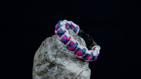 Photo for Braided paracord bracelet on a stone, on a black background. Handmade, creative design. - Royalty Free Image