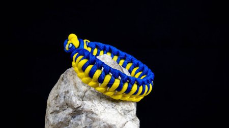 Photo for Braided paracord bracelet on a stone, on a black background. Handmade, creative design. - Royalty Free Image