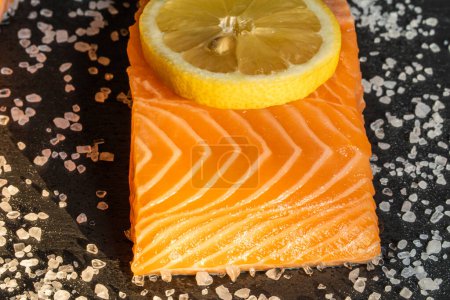 Téléchargez les photos : Vue de dessus du steak de saumon cru frais avec des épices sur un fond de pierre sombre. Sel, épices, assaisonnements et autres ingrédients. - en image libre de droit