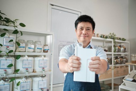 Photo for Portrait of Thai male shopkeeper smiles and looks at camera with reusable container, organic products at refill store, zero-waste grocery, and plastic-free, environment-friendly sustainable business. - Royalty Free Image