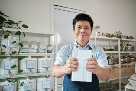 Photo for Portrait of Thai male shopkeeper smiles and looks at camera with reusable container, organic products at refill store, zero-waste grocery, and plastic-free, environment-friendly sustainable business. - Royalty Free Image