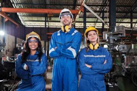 Foto de Industrial workers team in safety uniforms with confident arms crossed, engineering colleagues, work with metalwork machines in manufacturing factory. Professional production engineer occupation. - Imagen libre de derechos