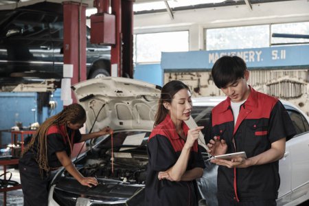 Two Asian professional mechanics, male supervisor engineer, and partner discuss and inspect repair work checklists at garage, service car maintenance, and fixing specialist occupations auto industry.