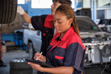 Photo for Young expert Black female inspects repair checklist with automotive mechanic worker partner, quality suspension technician team at fix garage. Vehicle maintenance service works industry occupation jobs. - Royalty Free Image