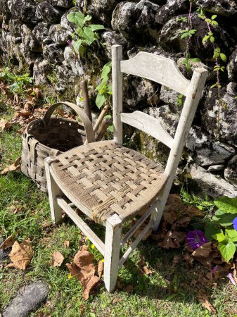 Una silla y una cesta de madera al lado de una pared, en un césped