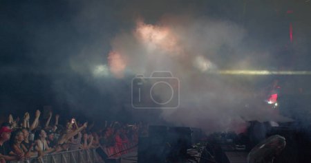 Photo for The movement smoke on stage flashes lights to the rhythm music, creating perceptual impression of the viewer fan blows smoke dynamic effect. Crowd spectators. CZ, Milovice, 6.8.22 Let it Roll - Royalty Free Image
