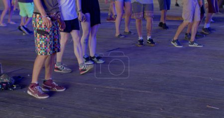 Photo for Learning to dance on the dance floor. The legs of the ravers make movements to the beat of the music. Learning new dance moves, body coordination training. CZ, Milovice, 7.8.22 Let it Roll - Royalty Free Image