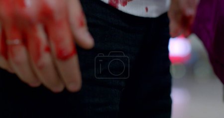 Photo for Red spots on a white T-shirt, bloody clothes after a street fight. The guy is waiting for help. Bowed his head, endure the pain, shock smile. - Royalty Free Image