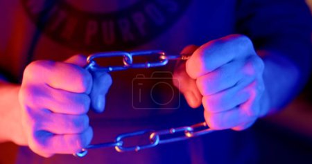 Foto de Tensioning the chain with the hands of a man in the light of police flashing lights. An illustration of the stiffness of life, holding itself back. Soft focus. - Imagen libre de derechos