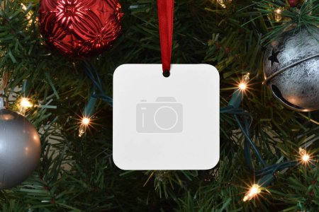 Photo for Closeup of a square white Christmas ornament dangling from a lit up Christmas tree. - Royalty Free Image