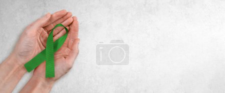 Téléchargez les photos : Photo de ruban vert dans les mains de la femme sur un fond de béton gris clair. Beaucoup d'espace de copie. - en image libre de droit