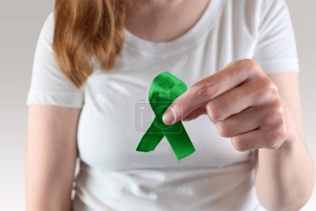 Foto de Mujer caucásica joven sosteniendo una cinta de conciencia verde para la salud mental y los meses de conciencia de glaucoma. - Imagen libre de derechos