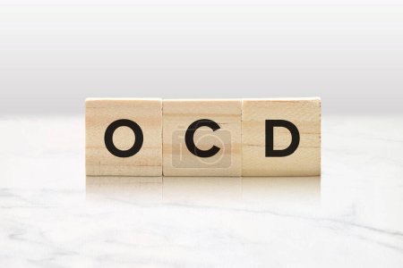 Drei Holzfliesen mit OCD-Buchstaben vor edlem weißem Marmorhintergrund.