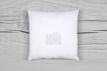 Photo for White throw pillow resting in style atop a light gray weathered wooden surface. - Royalty Free Image