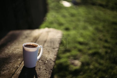 A cup of coffee stands on a wooden table in the garden