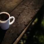 a cup of coffee stands on a wooden table in the garden