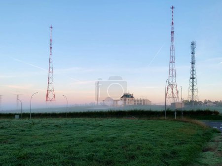 Foto de Junglinster Longwave Transmisor - tres torres de marco metálico de 215 m de altura en la niebla de la mañana temprano, y SES instalación de teletransporte con antenas parabólicas - Imagen libre de derechos