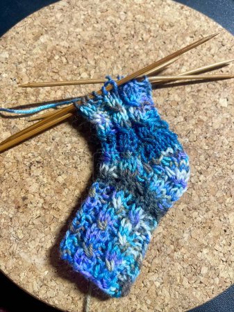 Photo for Knitting of a tiny sock in baby boy blue colour with wool yarn, on 5 short natural bamboo needles, twisted cable pattern, boomerang heel - Royalty Free Image