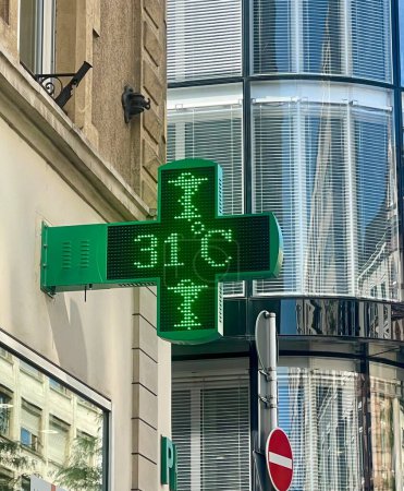 Foto de Signo de cruz verde de una farmacia hecha de diminutas luces led a la onda de calor que muestran la temperatura ambiente 31 grados Celsius - Imagen libre de derechos