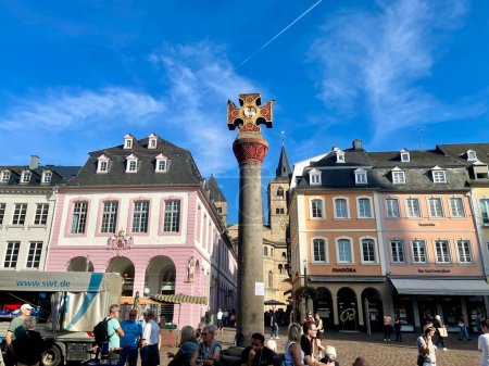 Photo for Oldest Market cross in Germany, with Latin dedication placed by Archbishop in 958, renovated 1724. Gothic houses with figures of saints behind it. Trier, Rhineland-Palatinate, Germany - September 14 - Royalty Free Image