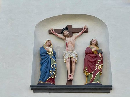 Mittelalterliches Kruzifix an der Fassade der Kirche St. Gangolf in Trier. Jesus am Kreuz und trauernde Mutter Maria und der heilige Johannes