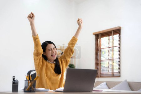 Foto de Emocionado mujer feliz mirando a la pantalla de la computadora portátil, celebrando una victoria en línea, lleno de alegría joven mujer asiática gritando de alegría en casa. - Imagen libre de derechos