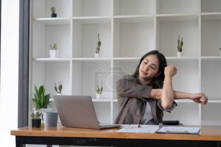 Photo for Asian businesswoman stretches her arms to relax her tired muscles from working at her desk all day at the office... - Royalty Free Image