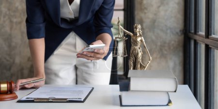Foto de Attractive young lawyer or Businesswoman talking on phone and lawyers discussing contract papers with brass scale on wooden desk in office. Law, legal services, advice, Justice and real estate concept - Imagen libre de derechos