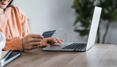 Young woman holding credit card and using laptop computer. Businesswoman working at home. Online shopping, e-commerce, internet banking, spending money, working from home concept..