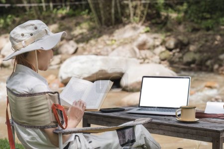 Téléchargez les photos : Jeune touriste dans la trentaine en vêtements safari assise dans une tente de camping et lisant un livre, activité de voyage en plein air Détendez-vous au milieu de la nature. - en image libre de droit