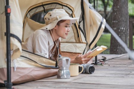Téléchargez les photos : Une jeune touriste dans la trentaine en tenue de safari se trouve dans une tente de camping et lit un livre. activités de voyage en plein air Détendez-vous dans la nature. - en image libre de droit